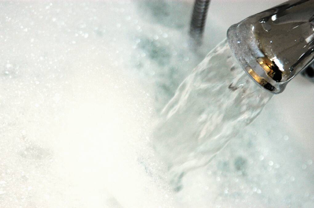 Water gushing from tap into bath containing bubble bath hot water